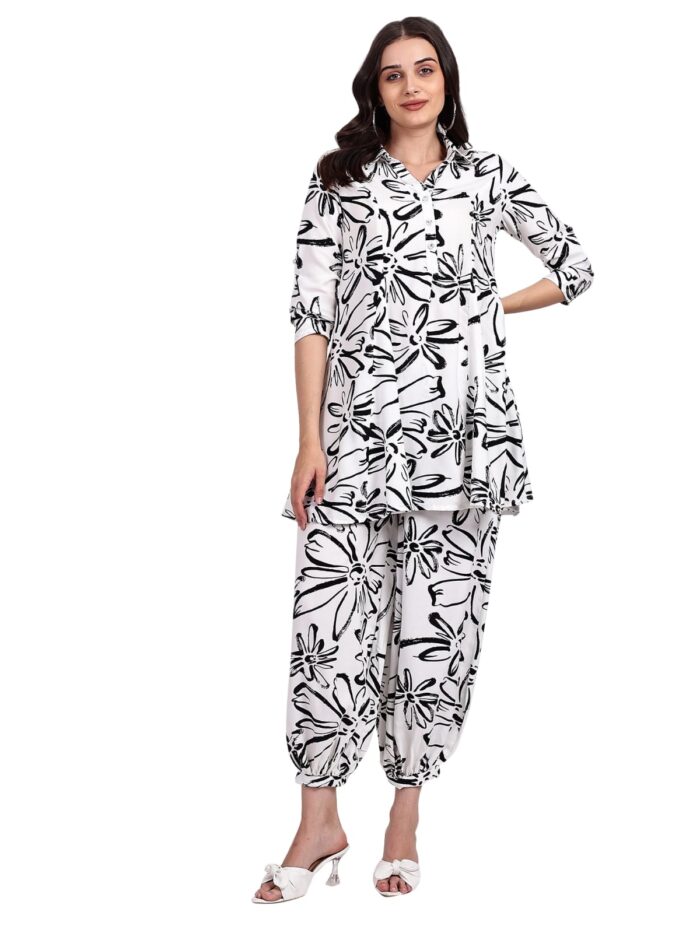 Woman wearing a white and black floral printed kurta with matching dhoti-style pants, paired with white heeled sandals, posing confidently.