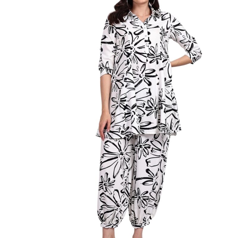 Woman wearing a white and black floral printed kurta with matching dhoti-style pants, paired with white heeled sandals, posing confidently.